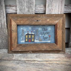 Peut inclure: Une broderie au point de croix encadrée représentant une scène hivernale avec une maison, des arbres et des flocons de neige. Le texte "Olde Wynter Tyme" est brodé au-dessus de la maison. Le cadre est en bois rustique et vieilli.