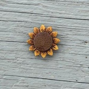 May include: A wooden sunflower with a brown center and yellow-orange petals. The sunflower is centered on a weathered, light blue-gray wooden surface.