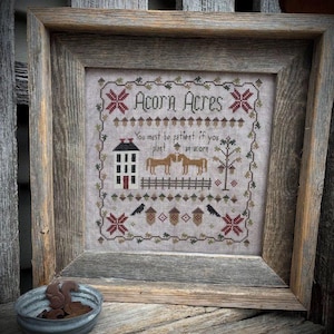 Puede incluir: Obra de arte de punto de cruz en un marco de madera rústico. El diseño presenta el texto "Acorn Acres" con una casa, caballos y bellotas. La obra de arte incluye la cita: "Hay que ser paciente si se planta una bellota."