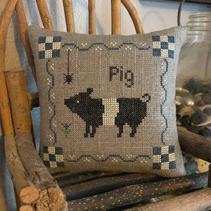 May include: A gray and white pillow with a black and white pig design and the word "Pig" embroidered on it. The pillow has a black and white checkered border.