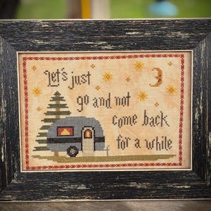 May include: Cross-stitch artwork in a black distressed frame. The design features a camper, tree, stars, and moon, with the text "Let's just go and not come back for a while."