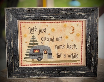 Könnte beinhalten: Kreuzstich-Kunstwerk in einem schwarzen, verwitterten Rahmen. Das Design zeigt einen Wohnwagen, einen Baum, Sterne und einen Mond mit dem Text "Let's just go and not come back for a while."