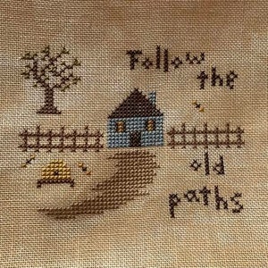 May include: Cross-stitch embroidery with a blue house, a tree, and a winding path. The text "Follow the old paths" is stitched in brown thread.