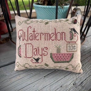 Peut inclure: Un coussin décoratif rectangulaire beige avec les mots "Watermelon Days" brodés en rouge. Le coussin présente des images brodées de pastèques, d'un oiseau et d'un vase de fleurs. Un petit panneau indique "10¢".