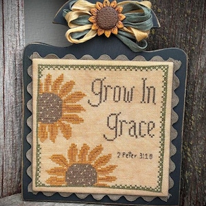 Peut inclure: Une broderie au point de croix encadrée avec un cadre noir et un bord festonné. La broderie représente deux tournesols et le texte "Grow in Grace 2 Peter 3:18".