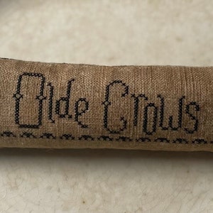 May include: A brown linen pillow with black embroidery of two crows and the text "Old Crows".