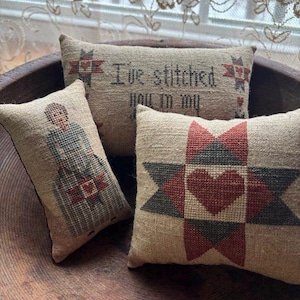 Peut inclure: Trois coussins décoratifs en toile de jute avec des motifs au point de croix. L'un des coussins porte le texte "I've stitched you in my" et des étoiles. Un autre présente un motif de cœur et d'étoile. Le troisième coussin a un motif de personnage.