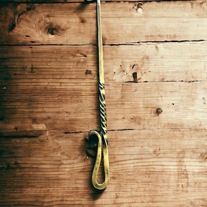 May include: A long, thin, metal fireplace poker with a twisted handle. The poker is hanging on a wooden wall.