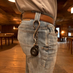 May include: A person wearing blue jeans with a brown leather belt and a silver key chain with a black remote attached.