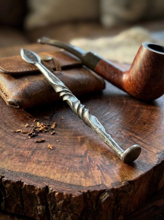 A blacksmith-forged one-piece steel pipe tamper and reamer — a niche, beautifully functional tool that can be personalized with initials or a date, making it a standout gift for pipe smokers.