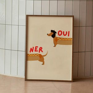 K&ouml;nnte beinhalten: Ein gerahmter Druck mit zwei Dackel-Illustrationen und den Worten "OUI" und "NER" in Rot. Eine Topfpalme steht in einer Ecke mit wei&szlig; gefliesten W&auml;nden und einem rosa Boden. Modernes Design.