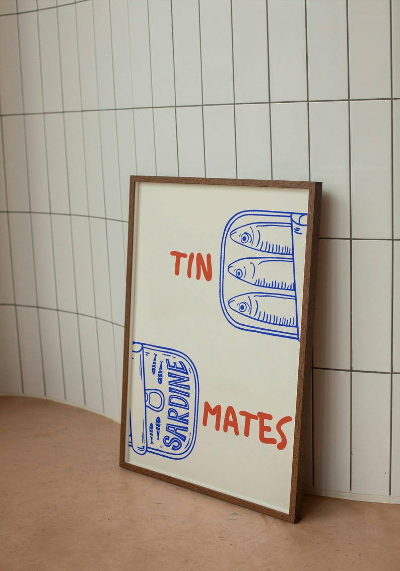 Pu&ograve; includere: Una stampa incorniciata con un'illustrazione di sardine in scatola. Il design utilizza blu e rosso, con le parole "TIN MATES". La cornice &egrave; marrone. L'opera d'arte raffigura sardine in scatola, con un carattere giocoso.