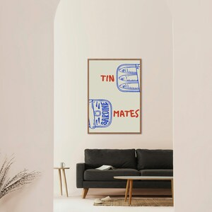 Pu&ograve; includere: Una stampa artistica incorniciata con un'illustrazione stravagante di scatole di sardine. L'opera d'arte include le parole "TIN" e "MATES" in rosso, con "SARDINE" in blu. L'immagine &egrave; su uno sfondo neutro.