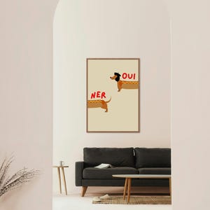 K&ouml;nnte beinhalten: Ein gerahmter Kunstdruck mit zwei Cartoon-Dackeln, die als Hotdogs gestaltet sind. Das Wort "OUI" steht &uuml;ber einem Hund, und "NER" steht &uuml;ber dem anderen. Der Hintergrund ist hellbeige.