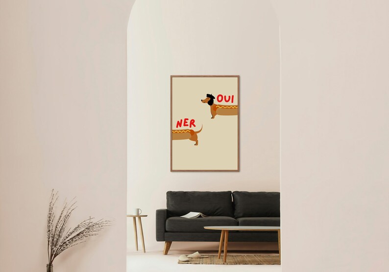 K&ouml;nnte beinhalten: Ein gerahmter Kunstdruck mit zwei Cartoon-Dackeln, die als Hotdogs gestaltet sind. Das Wort "OUI" steht &uuml;ber einem Hund, und "NER" steht &uuml;ber dem anderen. Der Hintergrund ist hellbeige.
