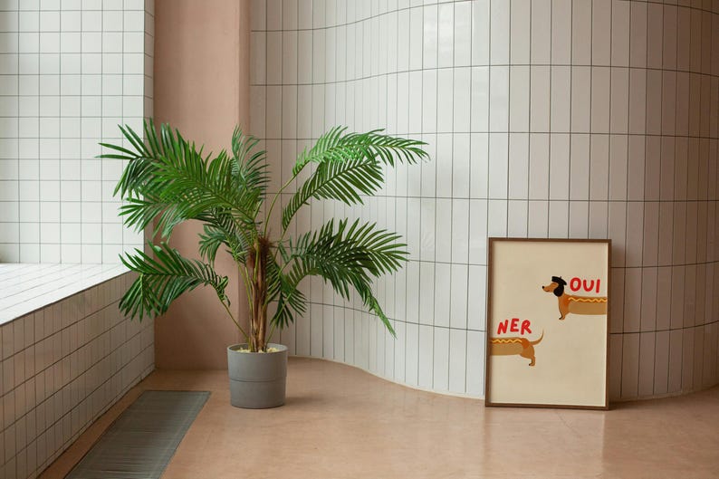K&ouml;nnte beinhalten: Ein gerahmter Druck mit zwei Dackel-Illustrationen und den Worten "OUI" und "NER" in Rot. Eine Topfpalme steht in einer Ecke mit wei&szlig; gefliesten W&auml;nden und einem rosa Boden. Modernes Design.