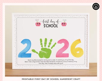 May include: A framed print with the words "first day of SCHOOL" above the numbers 2, a green handprint, and 26. The numbers are in blue, pink, and yellow watercolor. Text below reads "Here's my little handprint..." and "PRINTABLE FIRST DAY OF SCHOOL HANDPRINT CRAFT."