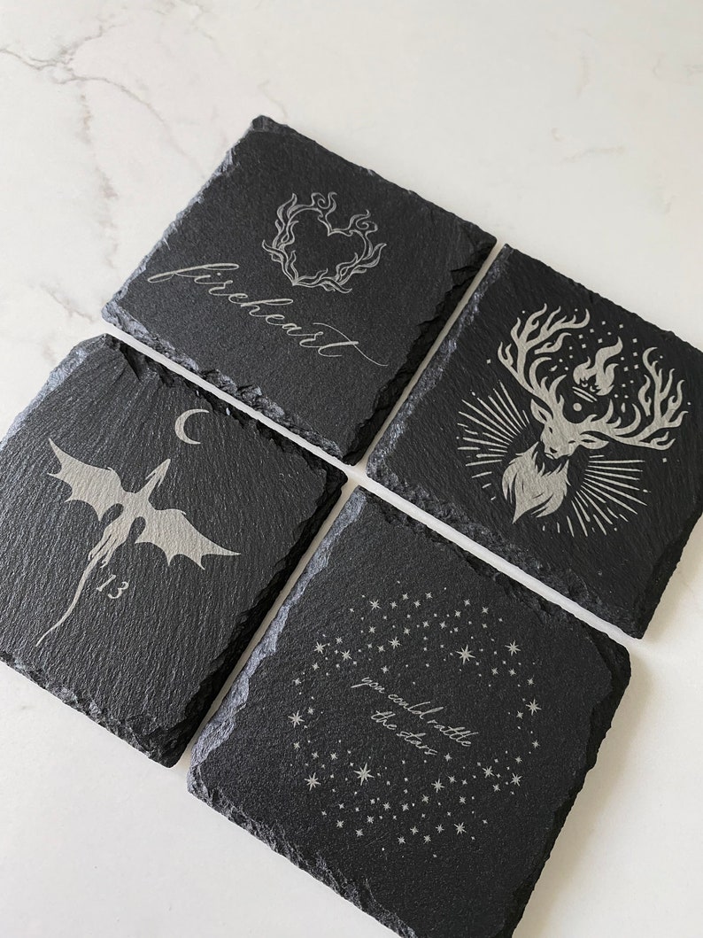 K&ouml;nnte beinhalten: Set aus vier schwarzen Schieferuntersetzern mit wei&szlig;en gravierten Designs. Die Designs beinhalten ein Herz mit Flammen, einen Hirsch mit Geweih, einen Drachen und eine Konstellation mit dem Text "Du k&ouml;nntest die Sterne zum Beben bringen".