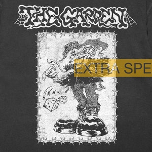 Puede incluir: Impresión gráfica en blanco y negro de un monstruo de dibujos animados con un borde de alambre de púas. El texto "THE GARDEN" está en la parte superior de la imagen. El texto "EXTRA SPE" es parcialmente visible en la parte inferior de la imagen.