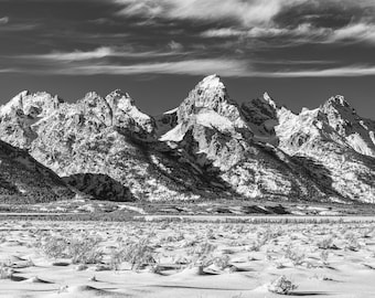 May include: A black and white photograph of a snow-capped mountain range with a cloudy sky. The mountains are tall and jagged, and the snow is pristine. The sky is filled with wispy clouds.