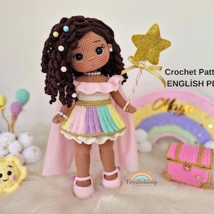 Puede incluir: Muñeca de ganchillo hecha a mano, cabello castaño, falda arcoíris, capa y zapatos rosas. La muñeca sostiene una varita de estrella dorada. El texto en la imagen dice "Crochet Pattern ENGLISH PDF". Un arcoíris y un cofre del tesoro rosa están en el fondo.