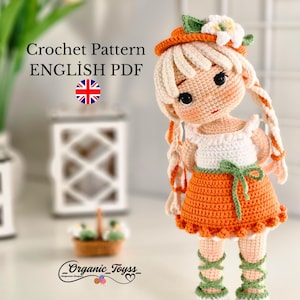 Könnte beinhalten: Häkelanleitung für eine Puppe mit orangefarbener und weißer Kleidung, einem weißen Hut mit grünen Blättern und blonden Haaren. Das Muster ist im englischen PDF-Format verfügbar. Die Puppe steht auf einer weißen Oberfläche.