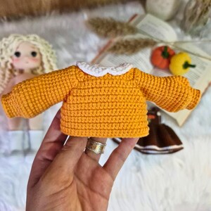 May include: A crocheted sweater for a doll, in a bright orange color with a white crocheted collar.