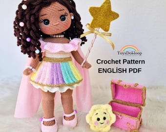 May include: A handmade crochet doll with brown hair adorned with colorful beads, wearing a pastel rainbow dress, pink cape, and shoes. The doll holds a gold star wand. Additional items include a small pink chest and a yellow sun-shaped item. The text "Crochet Pattern ENGLISH PDF" is visible.