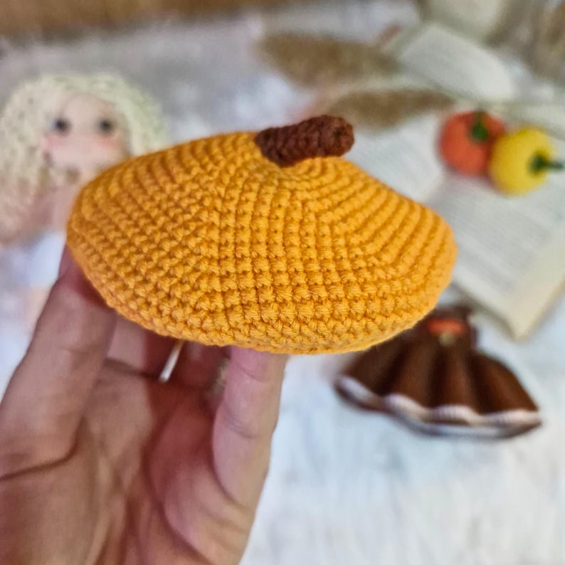 May include: A crocheted beret in a bright orange color. The beret has a small brown pom-pom on top.