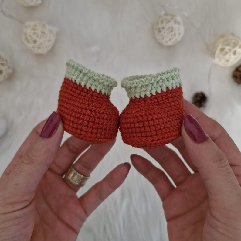 Op de afbeelding: Een paar kleine, gehaakte laarzen met een rood lichaam en een lichtgroene bovenkant.