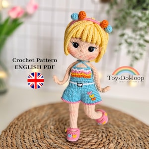 May include: A handmade crochet doll with blonde hair, wearing a blue outfit with pink accents. The doll has a smiling face and is standing on a woven mat. The text "Crochet Pattern ENGLISH PDF" is visible.