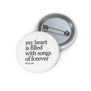 May include: White button with black text that reads "my heart is filled with songs of forever" and the word "thrice" below the text. The button has a silver back.