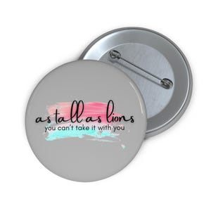 May include: A grey button with a pink and blue watercolour design and the text "as tall as lions you can't take it with you".