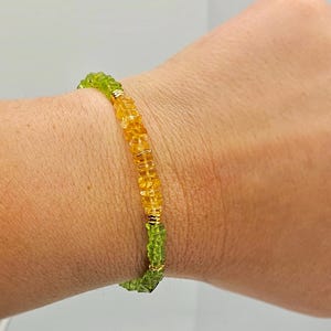 May include: A beaded bracelet featuring a mix of green and yellow gemstones. The bracelet is made with small, round beads and gold-colored accents. The gemstones are a vibrant green and yellow color.