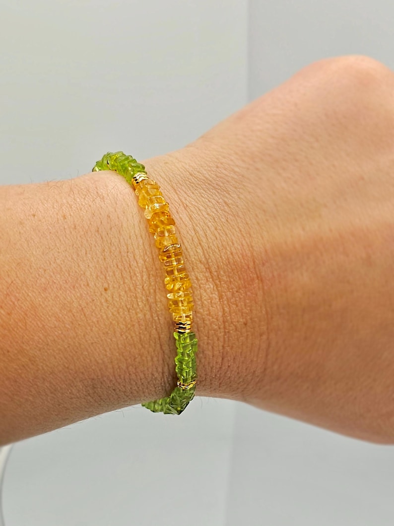 May include: A beaded bracelet featuring a mix of green and yellow gemstones. The bracelet is made with small, round beads and gold-colored accents. The gemstones are a vibrant green and yellow color.