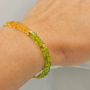 May include: A gemstone bracelet featuring a gradient of colors, transitioning from yellow-orange to green. The bracelet is composed of small, faceted beads and gold-colored accents. The jewelry is worn on a wrist.