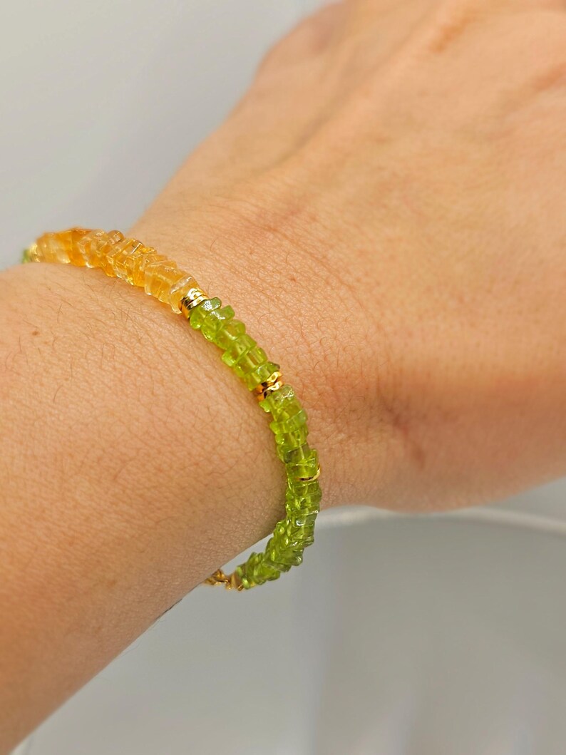May include: A gemstone bracelet featuring a gradient of colors, transitioning from yellow-orange to green. The bracelet is composed of small, faceted beads and gold-colored accents. The jewelry is worn on a wrist.