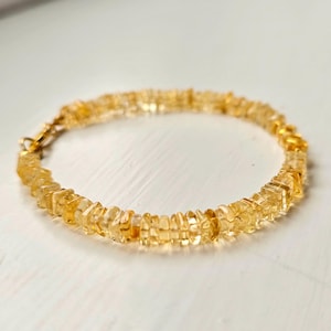 May include: A delicate bracelet featuring small, irregularly shaped, golden-yellow citrine beads. The bracelet is strung together with a gold-colored chain and clasp, creating a simple yet elegant piece of jewelry.