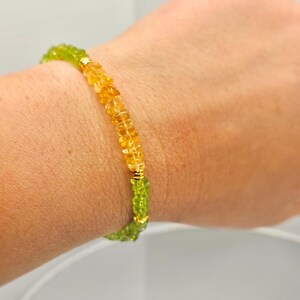 May include: A beaded bracelet featuring a combination of green and yellow gemstones. The bracelet is strung with small, faceted beads in shades of yellow and green, with gold-colored accents. The bracelet is worn on a wrist.