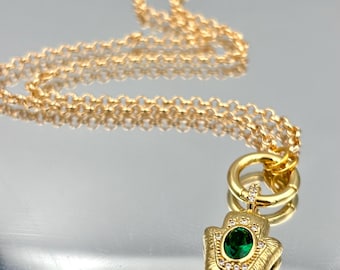 Peut inclure: Collier doré avec un pendentif en forme de main de Hamsa. Le pendentif est orné d'une pierre verte ovale et de pierres claires. La chaîne est délicate et à maillons. Le pendentif est détaillé avec des lignes texturées.