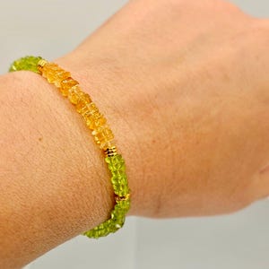 May include: A beaded bracelet featuring alternating sections of yellow and green gemstones. The bracelet is accented with gold-colored metal spacers. The gemstones are small and faceted, creating a sparkling effect. The bracelet is worn on a wrist.