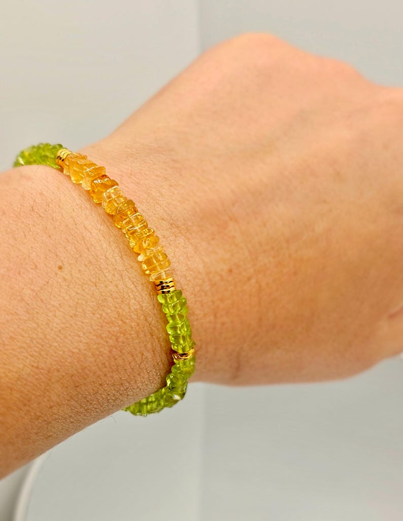 May include: A beaded bracelet featuring alternating sections of yellow and green gemstones. The bracelet is accented with gold-colored metal spacers. The gemstones are small and faceted, creating a sparkling effect. The bracelet is worn on a wrist.