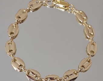 May include: A gold-colored bracelet featuring a series of oval-shaped links, connected to form a chain. The bracelet has a lobster clasp closure. The links have a smooth, polished surface, reflecting light. The jewelry is displayed on a reflective surface.