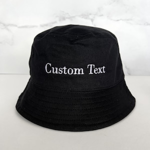 May include: A black bucket hat with white embroidery that says "Custom Text".