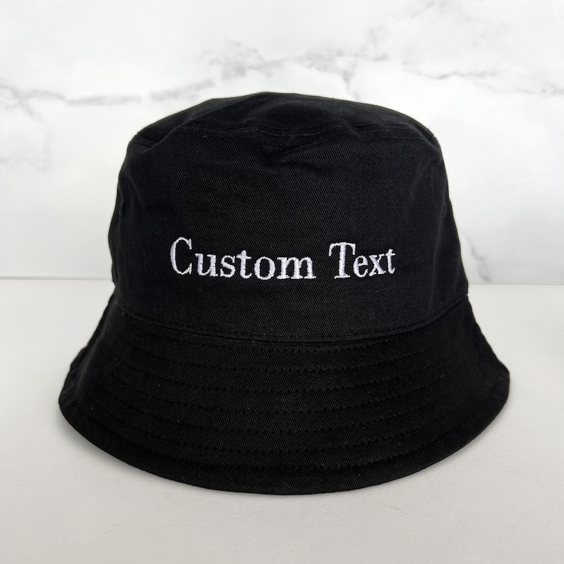 May include: A black bucket hat with white embroidery that says "Custom Text".