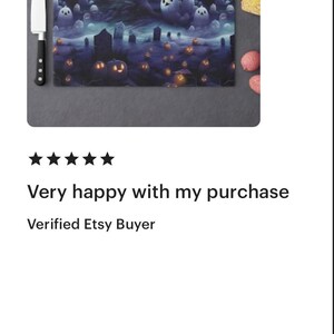 May include: A rectangular glass cutting board with a spooky Halloween design. The artwork features a haunted house, ghosts, and jack-o'-lanterns in a dark, eerie landscape. A chef's knife and some produce are next to the board.