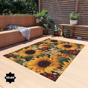 Puede incluir: Una alfombra rectangular con un diseño floral que presenta grandes girasoles amarillos, hojas verdes y flores blancas. La alfombra mide 60 pulgadas por 84 pulgadas.