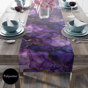 May include: Purple and gold abstract table runner with a marble-like design. The runner is made of polyester and is perfect for adding a touch of elegance to any dining table.