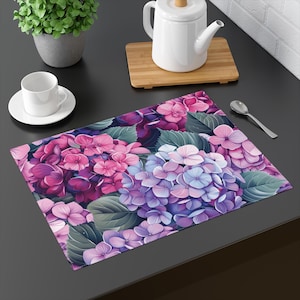 Puede incluir: Un mantel individual floral con un patrón de hortensias rosas, moradas y azules. El mantel individual está hecho de un material duradero y es perfecto para agregar un toque de elegancia a cualquier mesa de comedor.