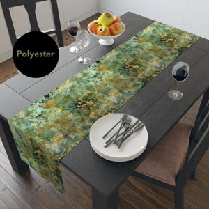 Könnte beinhalten: Ein grüner und goldener Tischläufer mit floralem Muster. Der Läufer ist aus Polyester und 35,5 cm breit. Er liegt auf einem dunklen Holztisch mit einem Satz weißer Teller und Besteck.